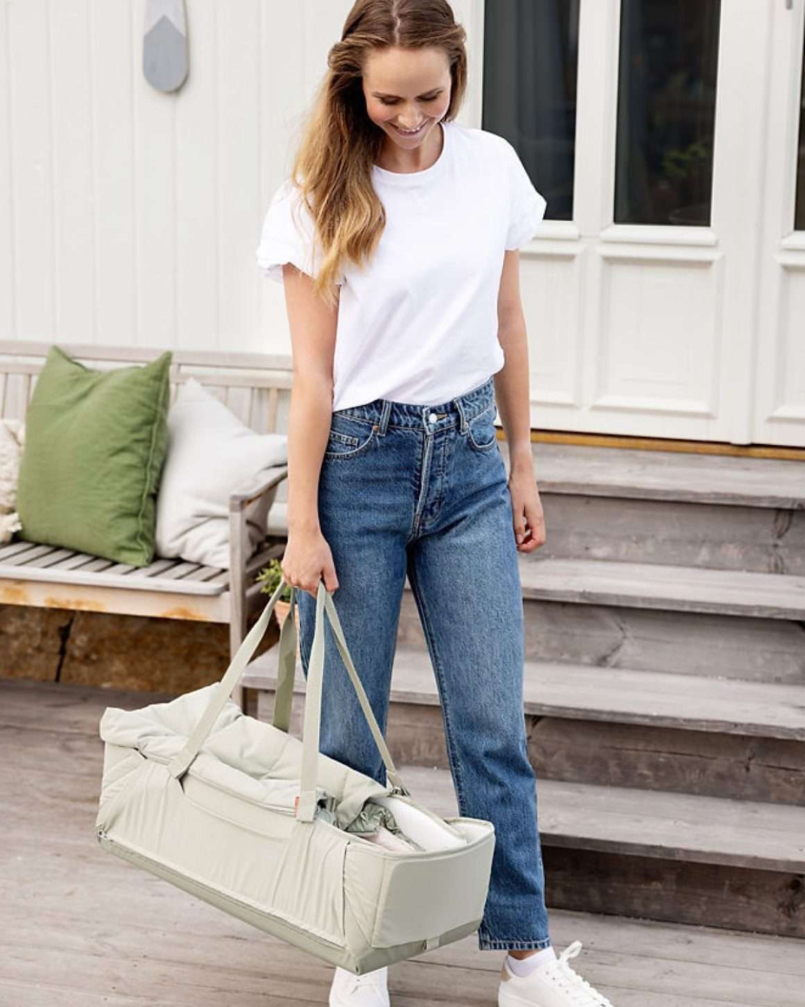 Dame bærer på en baby i Voksi Babylift Carry Me. Babynest med håndtak som er formet som en liten vognbag. Fargen på Babyliften er mintgrønn.