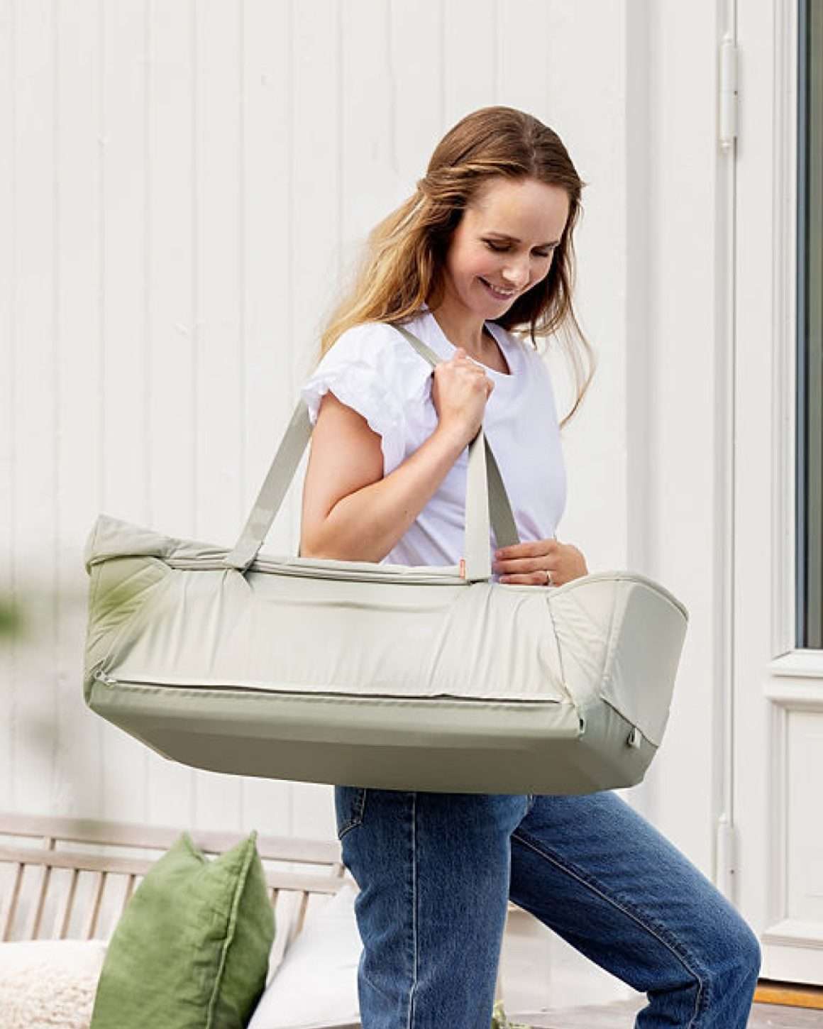 Dame bærer en Voksi Carry Me Babylift over skulderen. Et firkantet 3-i-1 babynest med håndtak som ser ut som en liten vognbag i formen. 
