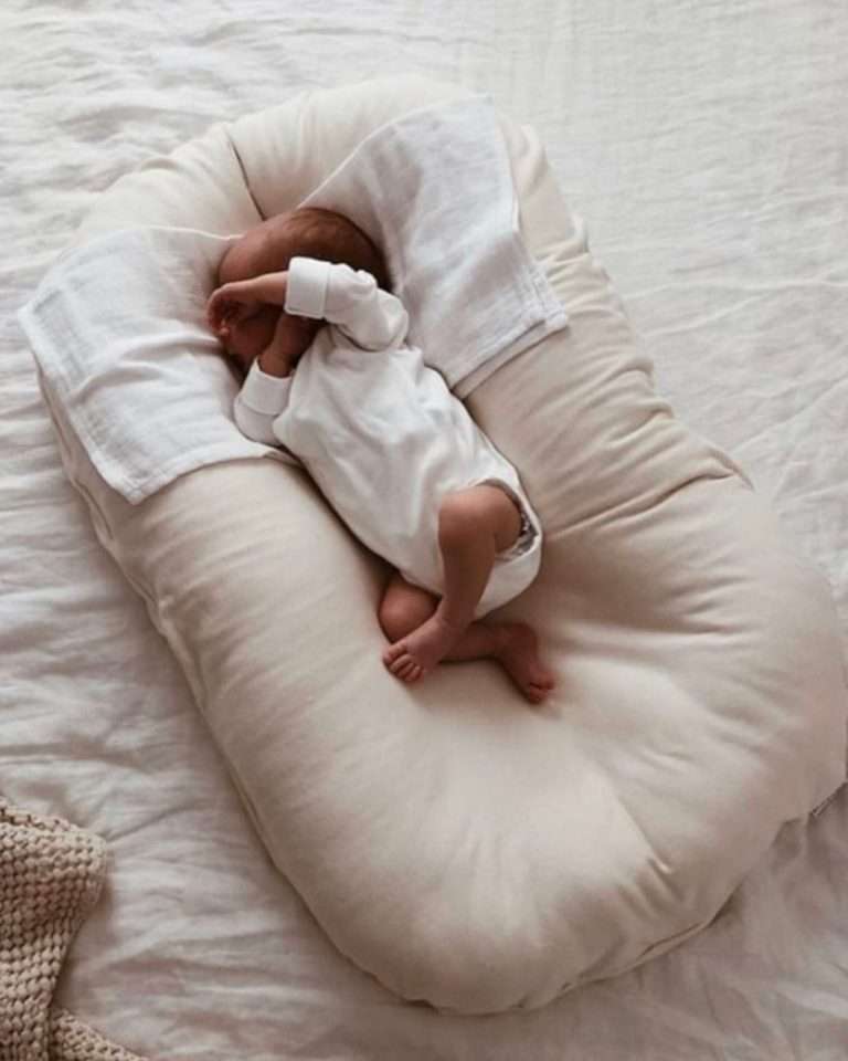 Ganske så nyfødt baby ligger og sover i et stilrent og kremhvitt babynest. Babynest er i en naturlig bomullsfarge