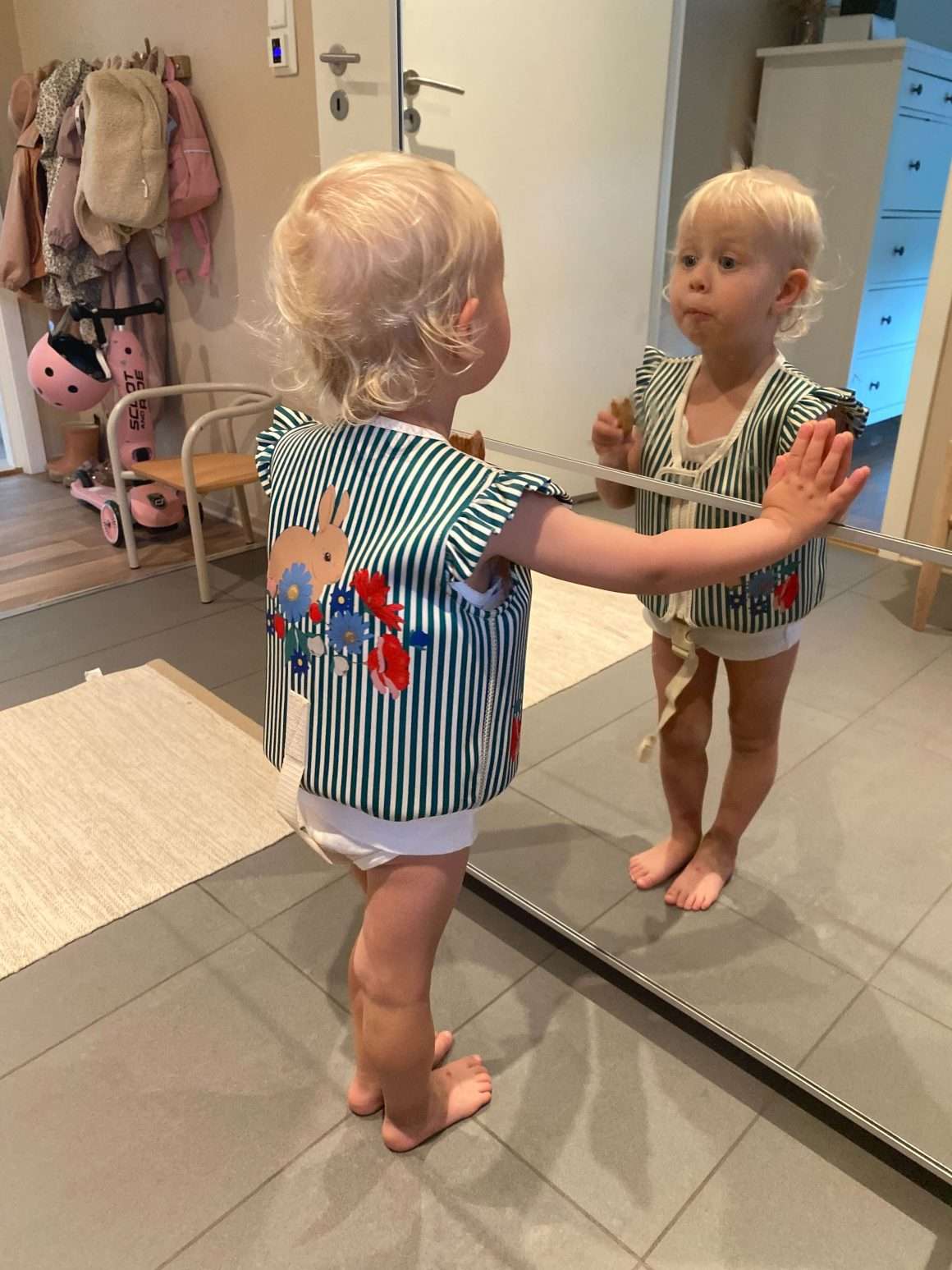 Lite barn har på seg en flytevest io feminint design med volang på skuldrene. Svømmevest fra KOnges Sløjd i grønne og hvite striper med motiv av kanin på ryggen.