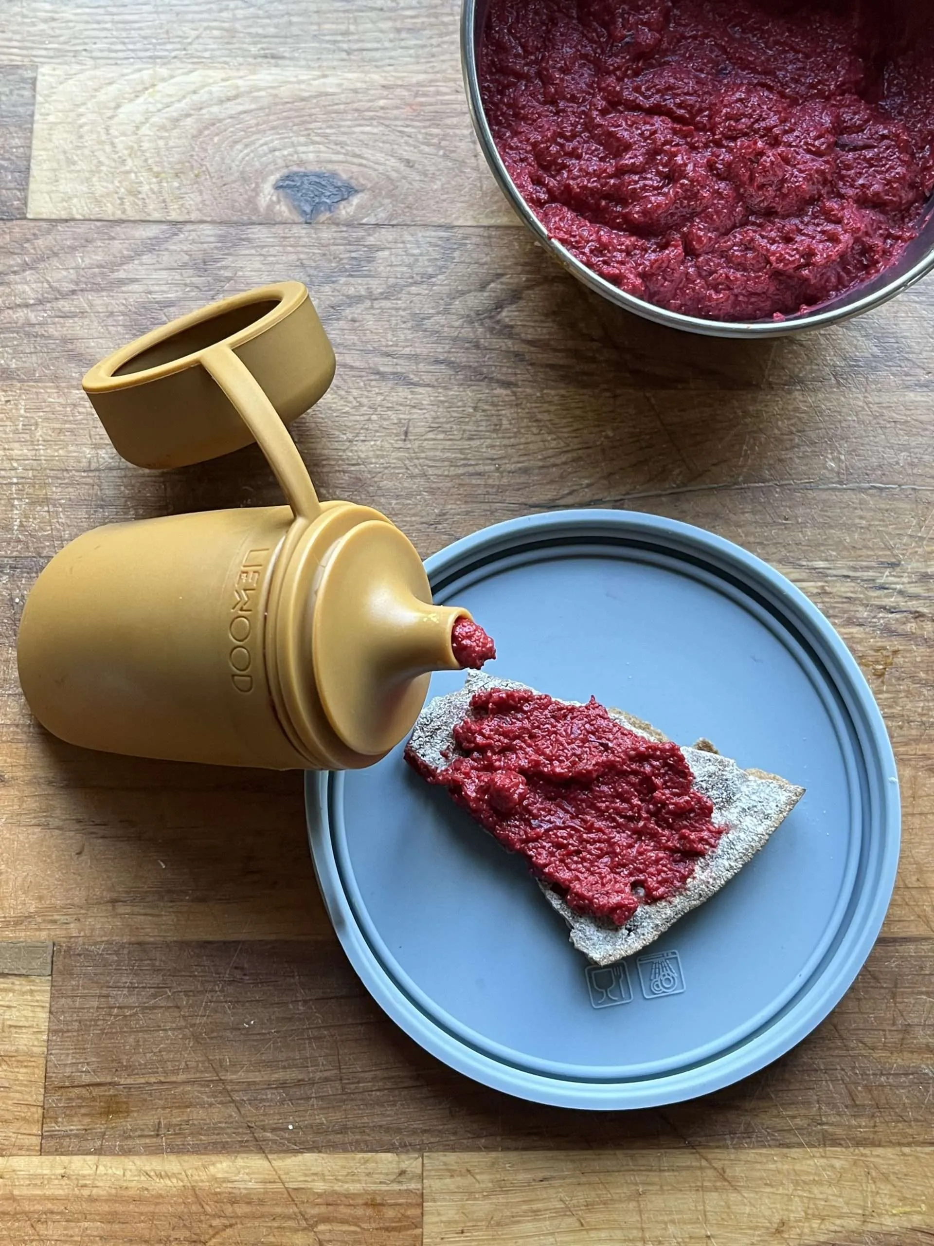 rosa pålegg oppi en Liewood klemmepose og Liewood matboks. Det ligger et knekkebrød med pålegget ved siden av.